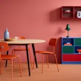 Ein Essbereich mit orangefarbenen Stühlen und einem Holztisch vor einer korallenroten Wand. Die Wandfarbe erinnert daran, wie man dunkelrot mischt.
