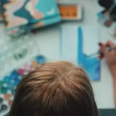 Kind malt mit Aquarellfarben. Die Palette zeigt viele Farben, aber wie mischt man braun?