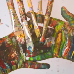 Bunte Hände und Pinsel, die zeigen, wie man grau mischt, indem man alle Farben übereinanderlegt.