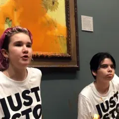 Zwei junge Menschen mit T-Shirts "JUST STOP" vor einem beschmierten Van Gogh Gemälde.