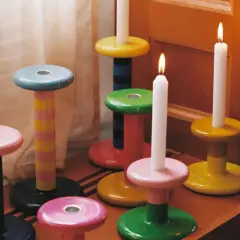 Bunte Kerzenständer in verschiedenen Formen und Farben, einige mit brennenden Kerzen.