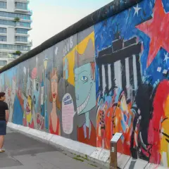 Bunte East Side Gallery in Berlin mit Graffiti und Menschen, im Hintergrund ein modernes Hochhaus.