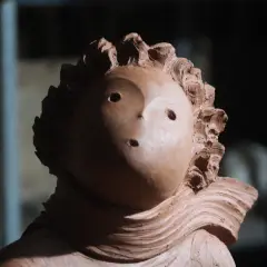 Ton-Skulptur eines Kopfes mit welligem Haar und zwei Augenlöchern.