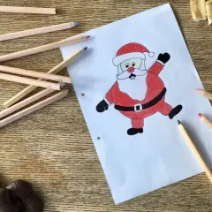Buntstiftzeichnung eines lachenden Nikolaus auf Papier, umgeben von Buntstiften und Keksen.