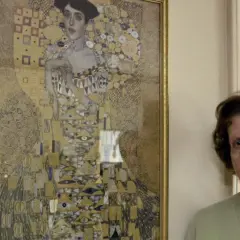 Eine ältere Frau steht neben Gustav Klimts "Adele Bloch-Bauer I", einem goldenen Porträt mit geometrischen Mustern.