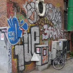 Ziegelwand mit Graffiti, Fahrrad und grauen Kästen.