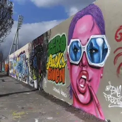 Bunte Graffiti-Wand mit Porträt einer Frau mit pinker Haut und blauen Sonnenbrillen.