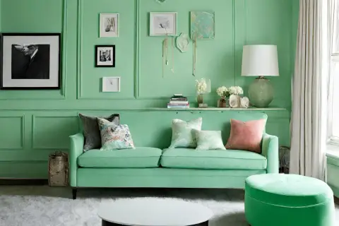 Ein Wohnzimmer in Mintgrün, das zeigt, wie man Mintgrün mischt. Ein grünes Sofa mit Kissen, ein runder Hocker und Kunst an der Wand.