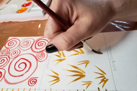 Hand malt mit Pinsel und Aquarellfarben, zeigt verschiedene Duktus-Beispiele wie Spiralen und Striche.