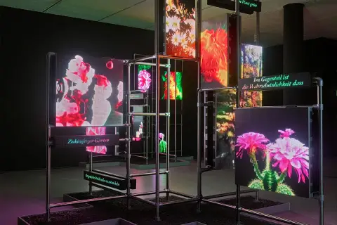 Installation mit leuchtenden Bildschirmen, die Blumen und Texte zeigen. Deutsche Künstler präsentieren einen "Zukünftigen Garten".