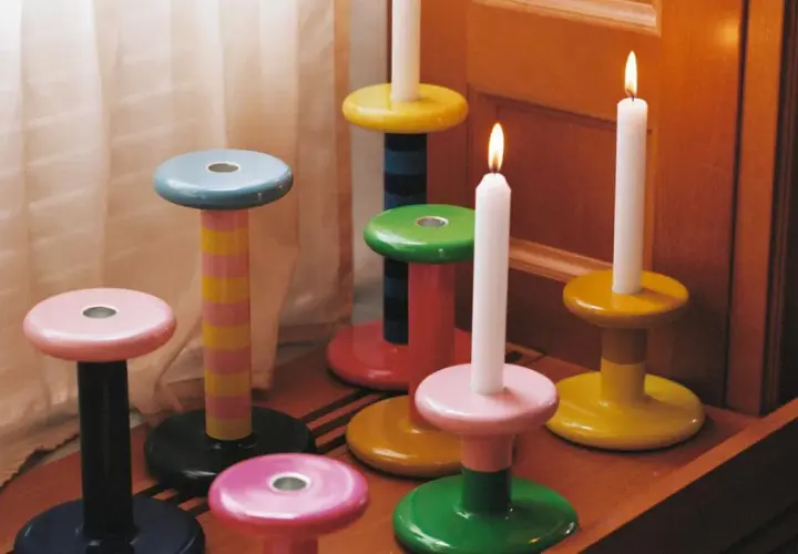 Bunte Kerzenständer in verschiedenen Formen und Farben, einige mit brennenden Kerzen.