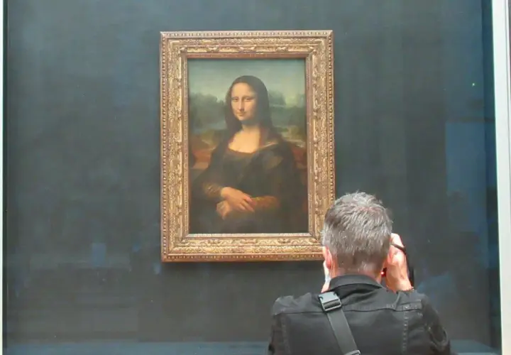 Ein Mann fotografiert die Mona Lisa. Die Frage, wie lange hat Da Vinci für die Mona Lisa gebraucht, beschäftigt viele Besucher.