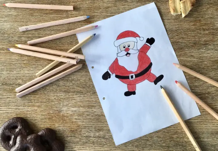 Buntstiftzeichnung eines lachenden Nikolaus auf Papier, umgeben von Buntstiften und Keksen.