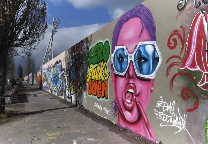 Bunte Graffiti-Wand mit Porträt einer Frau mit pinker Haut und blauen Sonnenbrillen.