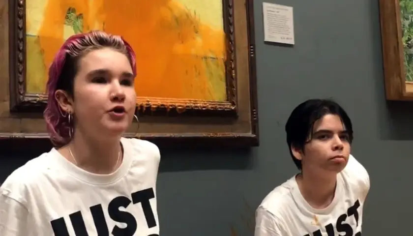 Zwei junge Menschen mit T-Shirts "JUST STOP" vor einem beschmierten Van Gogh Gemälde.