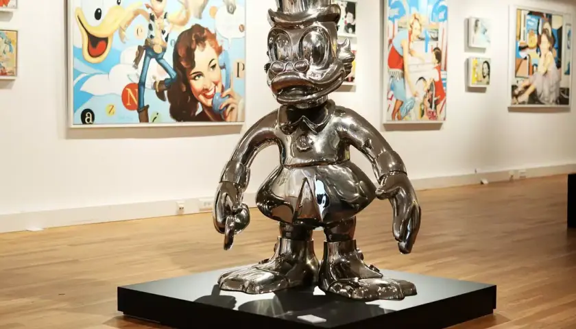 Glänzende Pop-Art-Skulptur einer Comicfigur mit Zylinder in einer Galerie, im Hintergrund bunte Gemälde.