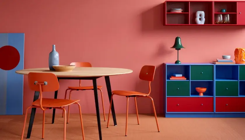 Ein Essbereich mit orangefarbenen Stühlen und einem Holztisch vor einer korallenroten Wand. Die Wandfarbe erinnert daran, wie man dunkelrot mischt.