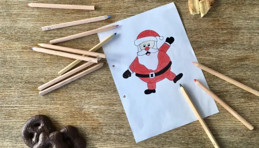 Buntstiftzeichnung eines lachenden Nikolaus auf Papier, umgeben von Buntstiften und Keksen.