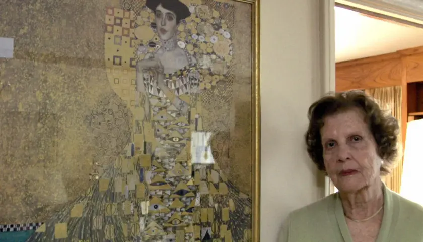 Eine ältere Frau steht neben Gustav Klimts "Adele Bloch-Bauer I", einem goldenen Porträt mit geometrischen Mustern.