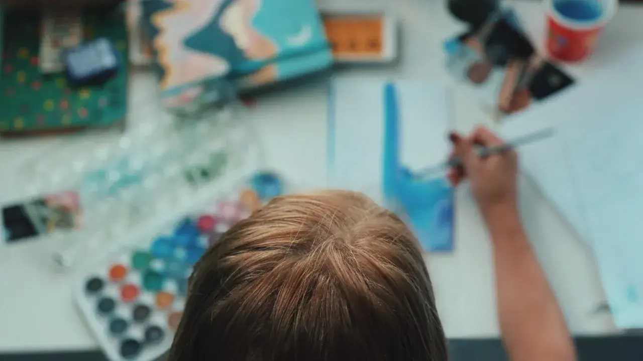 Kind malt mit Aquarellfarben. Die Palette zeigt viele Farben, aber wie mischt man braun?