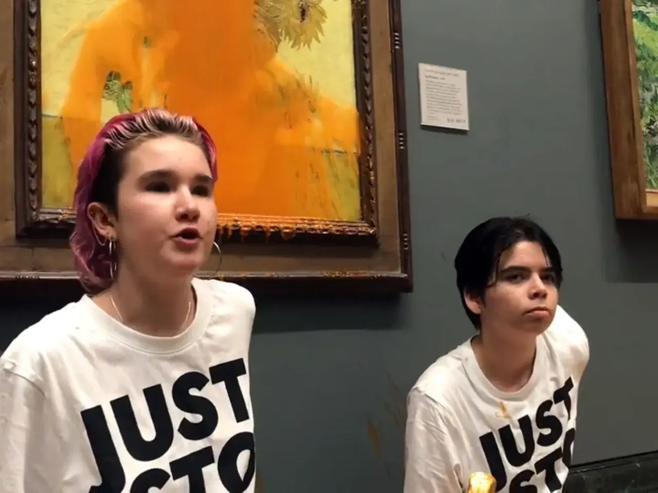 Zwei junge Menschen mit T-Shirts "JUST STOP" vor einem beschmierten Van Gogh Gemälde.