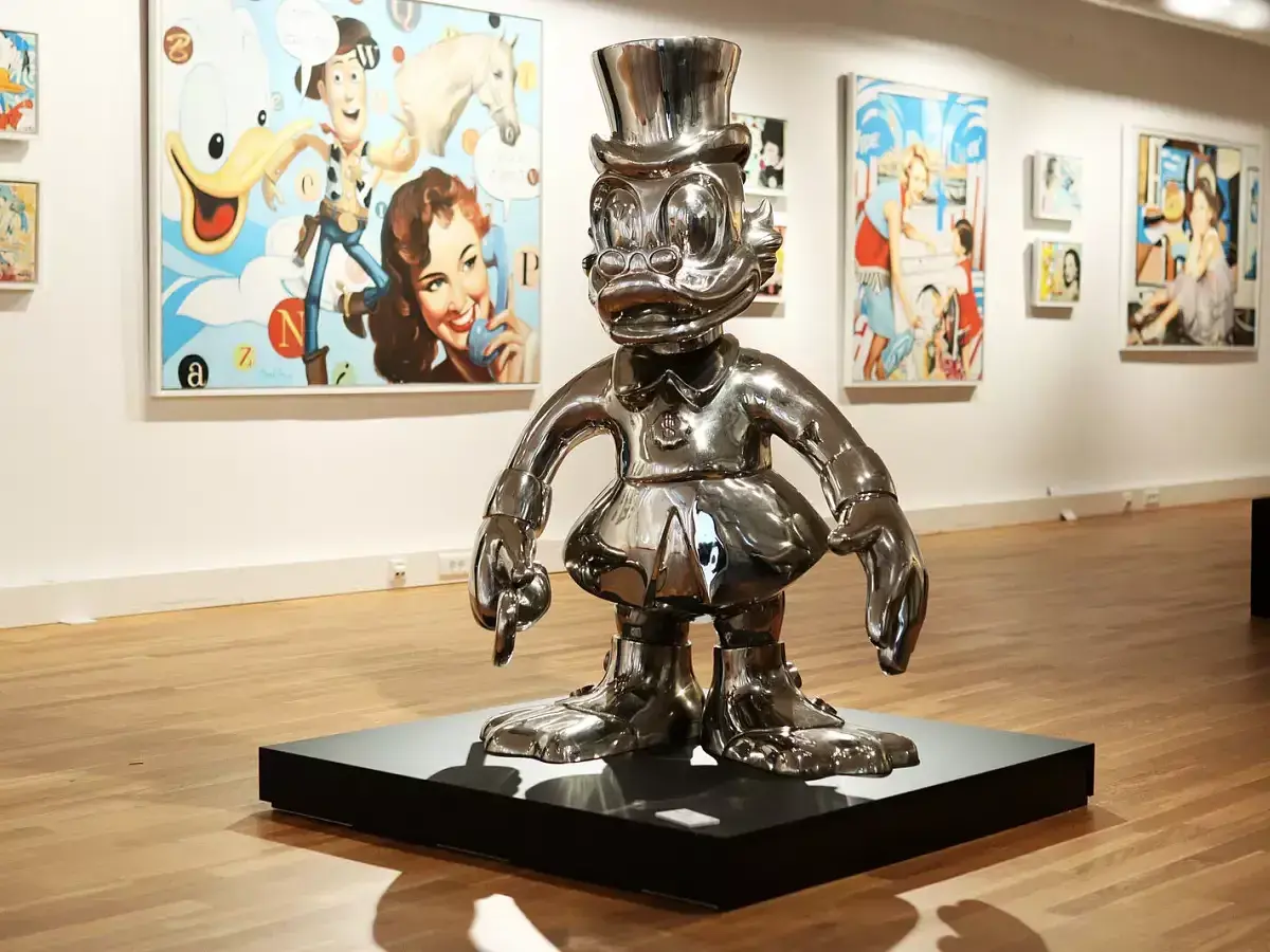 Glänzende Pop-Art-Skulptur einer Comicfigur mit Zylinder in einer Galerie, im Hintergrund bunte Gemälde.