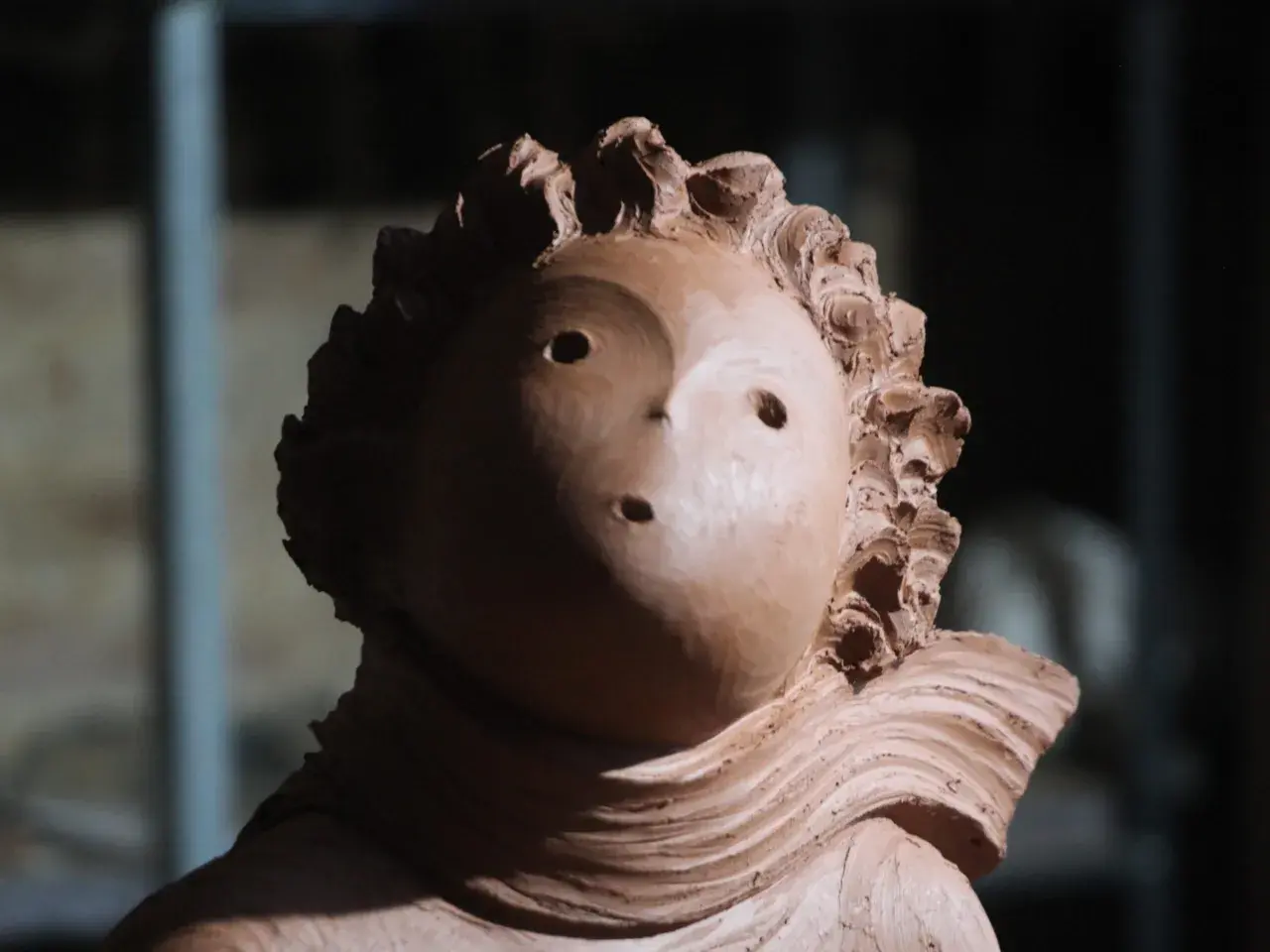 Ton-Skulptur eines Kopfes mit welligem Haar und zwei Augenlöchern.