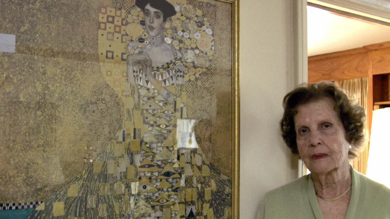 Eine ältere Frau steht neben Gustav Klimts "Adele Bloch-Bauer I", einem goldenen Porträt mit geometrischen Mustern.