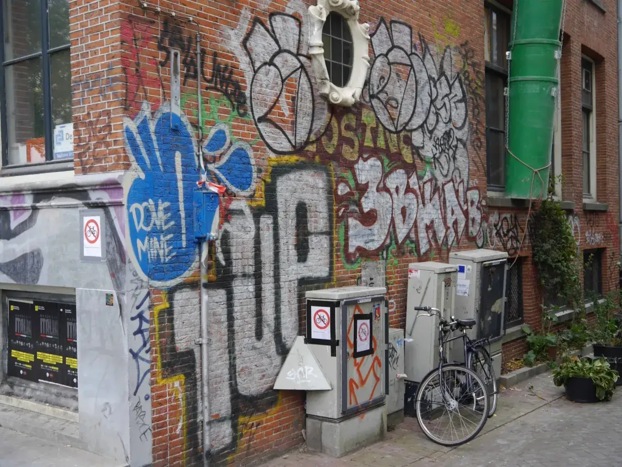 Ziegelwand mit Graffiti, Fahrrad und grauen Kästen.