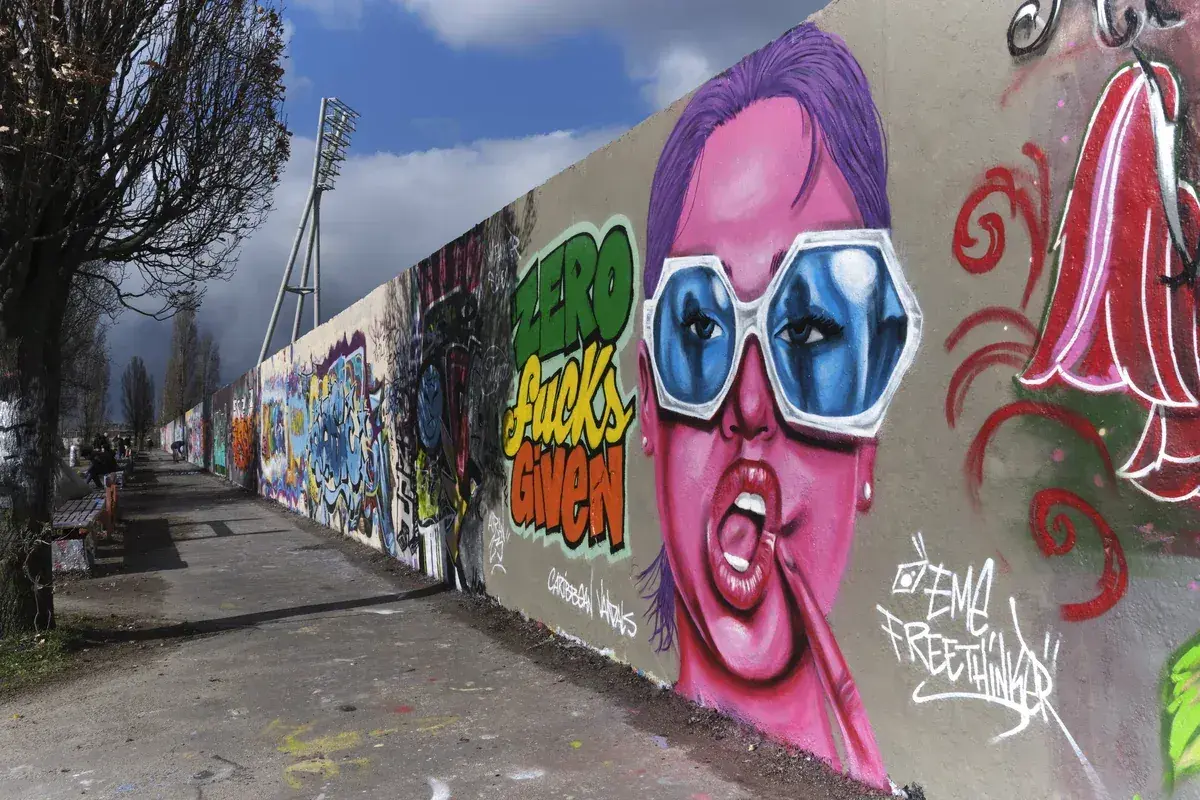 Bunte Graffiti-Wand mit Porträt einer Frau mit pinker Haut und blauen Sonnenbrillen.