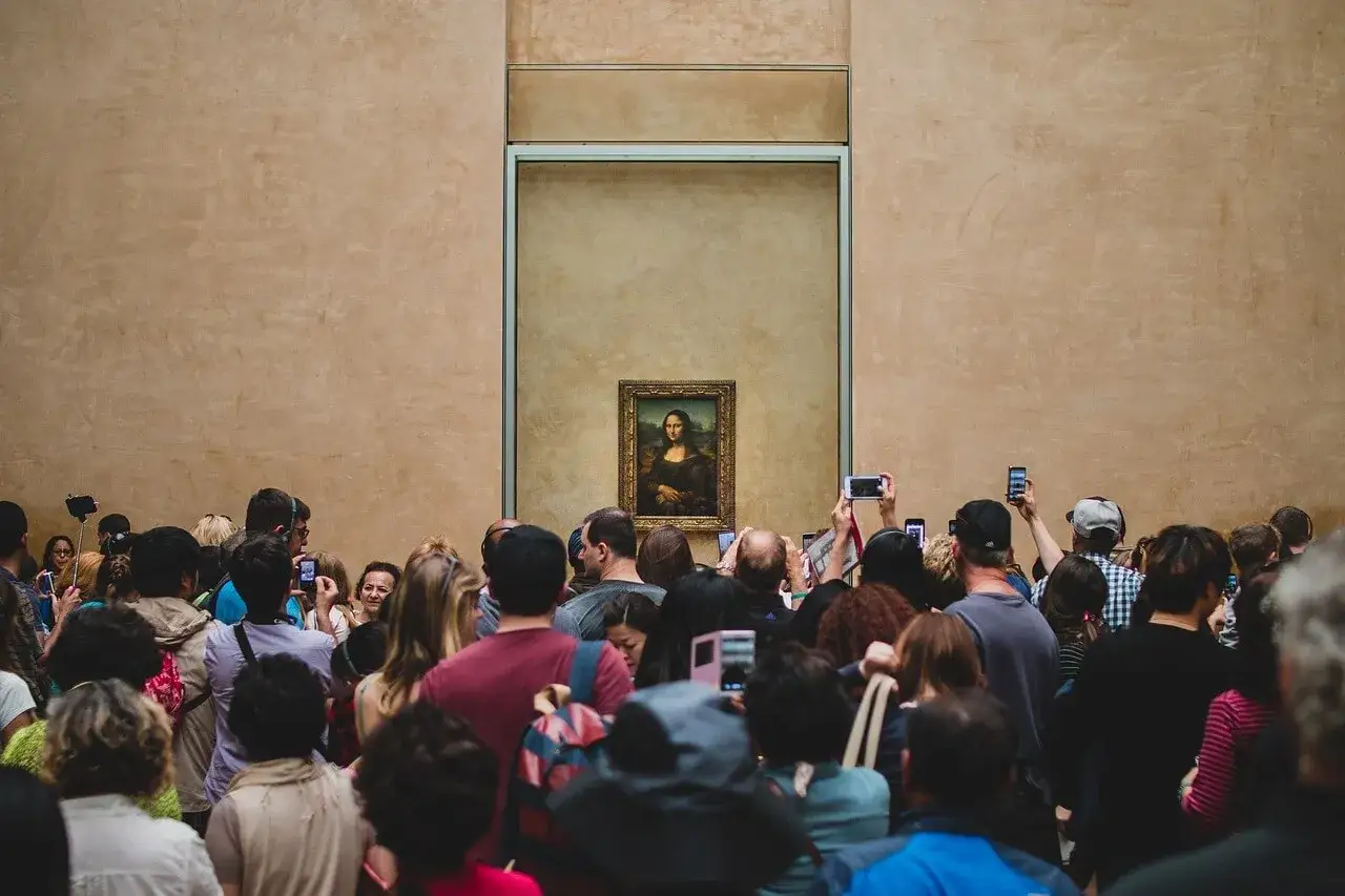Menschenmassen bestaunen das Mona Lisa Bild original im Louvre. Viele halten Handys hoch, um das berühmte Kunstwerk zu fotografieren.