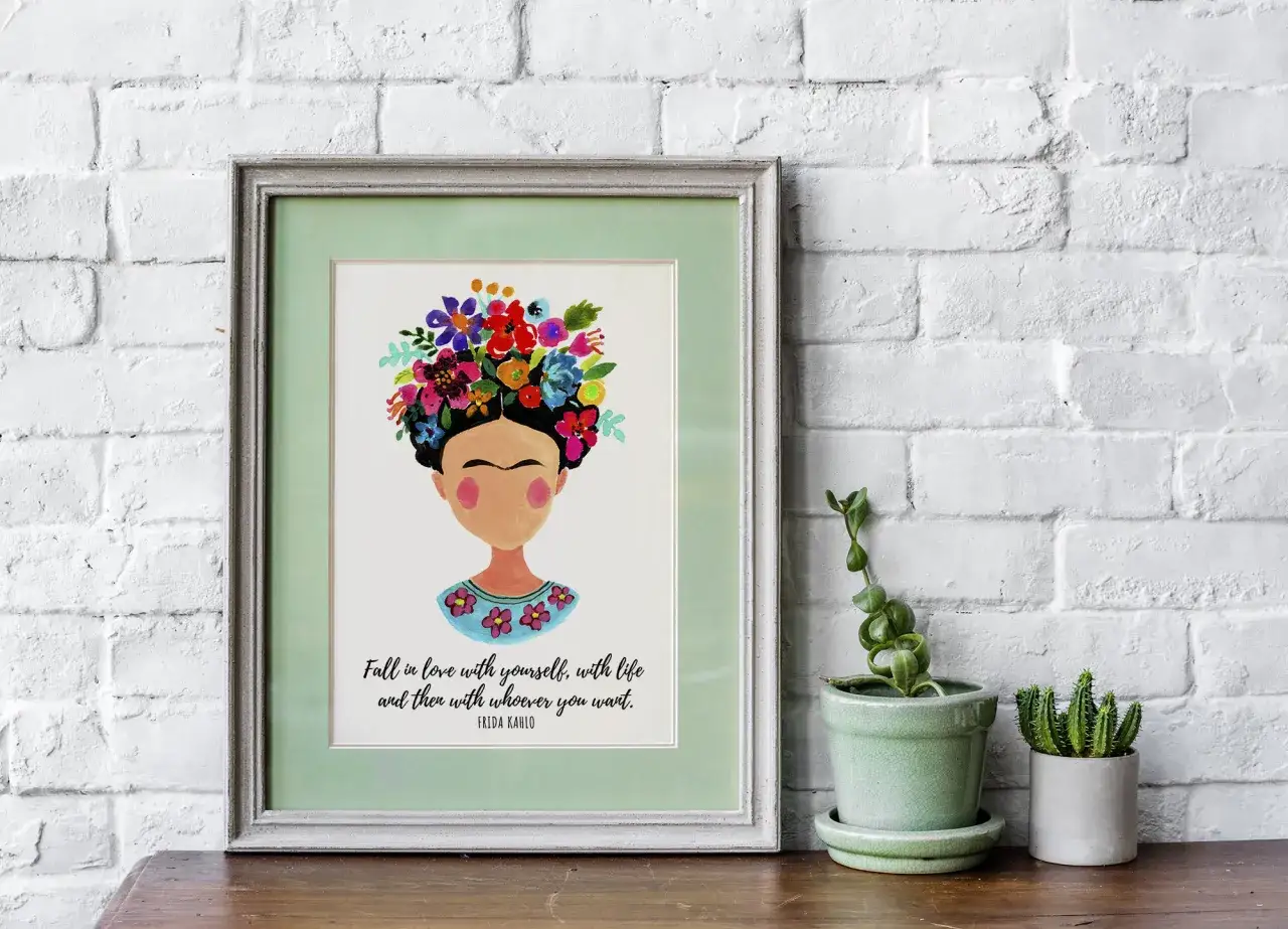 Gerahmtes Bild mit Frida Kahlo und einem Zitat über Selbstliebe. Ein inspirierendes Stück, das an einer weißen Ziegelwand hängt.